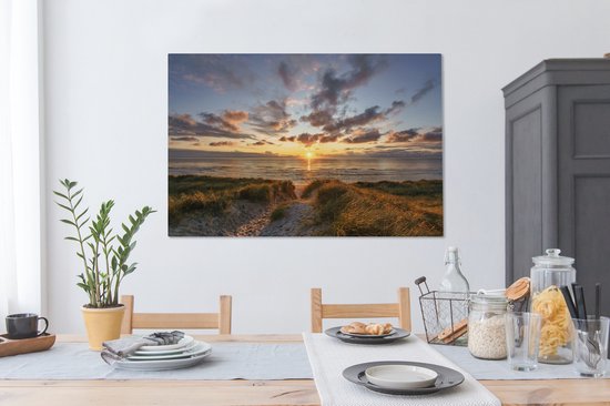 Salle à manger avec table en bois et sur le mur une toile d'un coucher de soleil sur les dunes.
