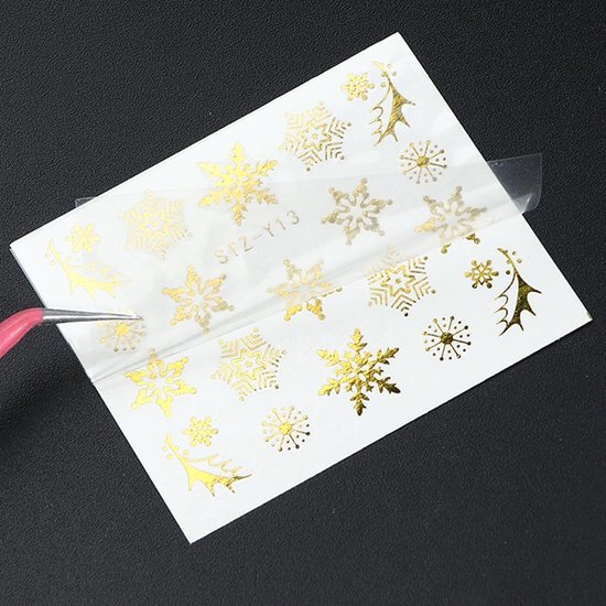 Een vel met gouden nail art stickers, met diverse maten sneeuwvlokken en kerstachtige takjes.