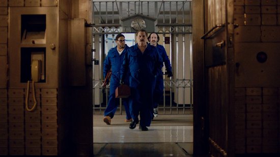 Drie mannen in blauwe overalls, lopen door een bank met kluisdeuren en kluisjes.