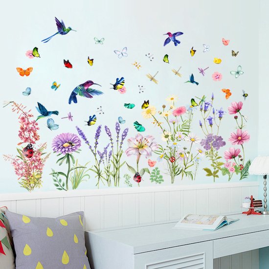 Décoration murale avec des fleurs, des papillons et des colibris sur un mur bleu clair, au-dessus d'un bureau avec un coussin gris.