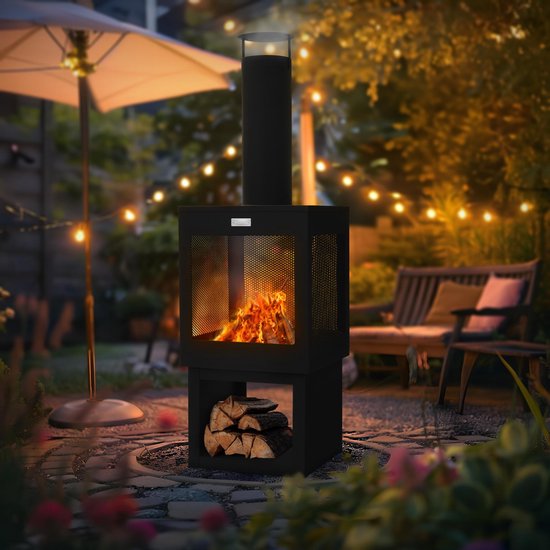 Zwarte tuinhaard met gloeiend vuur en houtopslag in een sfeervolle tuin met verlichting en tuinmeubilair.