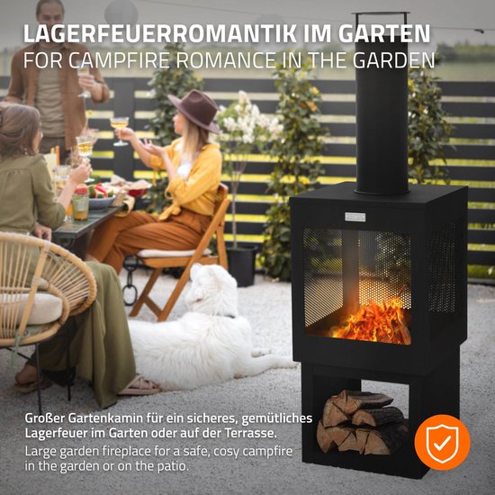 Gezellige tuin scène met een zwarte tuinhaard, met brandend vuur, houtopslag en mensen die genieten aan een tafel.