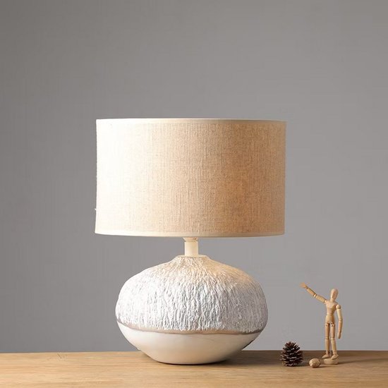 Wit met textuur tafellamp met linnen kap. Een decoratieve houten figuur staat ernaast.