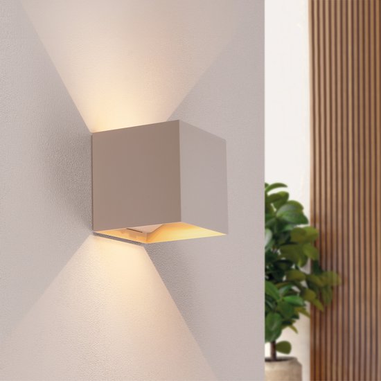 Applique murale moderne beige en forme de cube projetant une lumière chaude vers le haut et le bas.