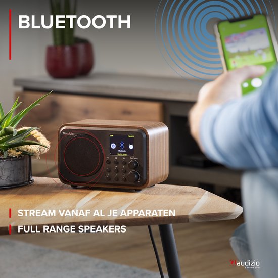 DAB radio met houten behuizing, zwart front en display. Een persoon streamt muziek via Bluetooth vanaf smartphone.
