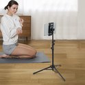 Vrouw in sportkleding knielt op een mat, met een tablet op een driepootstandaard ernaast.