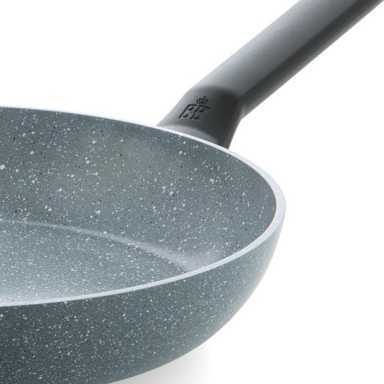 Detailopname van een grijze koekenpan met spikkelpatroon en zwart handvat met logo.