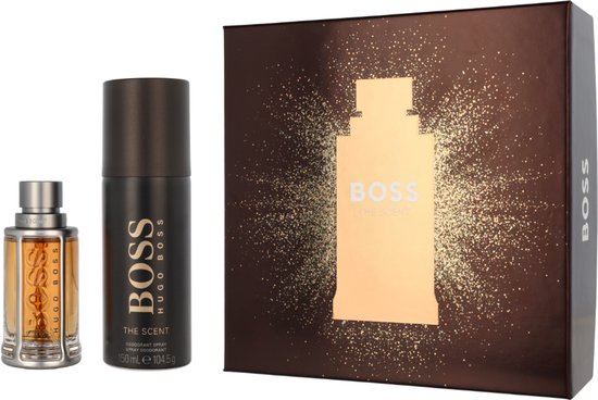 Een amberkleurig flesje eau de toilette en een zwarte deodorant spray, naast een geschenkdoos met "BOSS THE SCENT" erop.