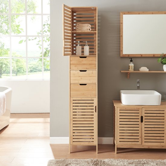 Badkamer met een hoge bamboe kast, wastafelmeubel en spiegel. Hoge kast heeft open deur met handdoeken en zeepjes.