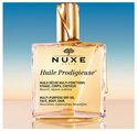 Gouden Nuxe Huile Prodigieuse multi-purpose dry oil in een glazen fles met gouden dop, op een achtergrond met blauwe lucht.
