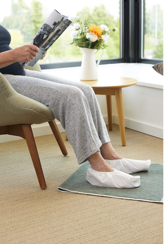 Een vrouw met grijze broek leest een tijdschrift met witte Swash Foot Caps aan haar voeten.