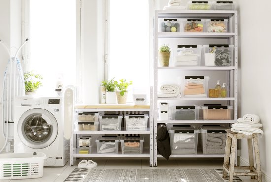 Woonkamer met opbergrekken vol met georganiseerde dozen, een wasmachine en een droogrek.