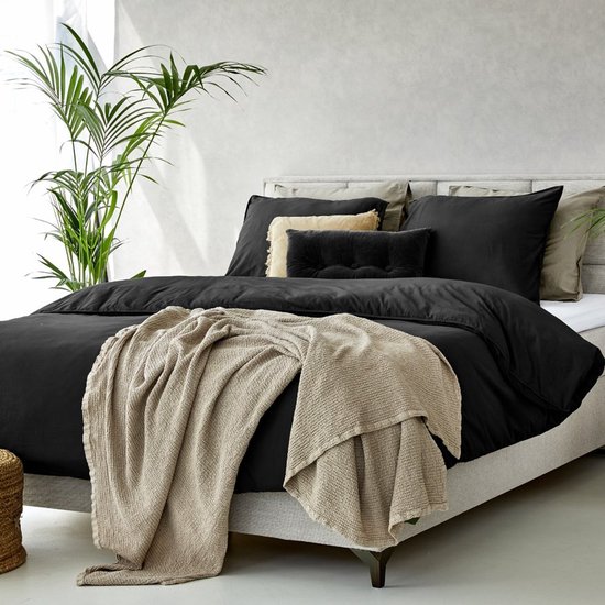 Housse de couette noire avec coussins décoratifs et plaid beige, sur un lit avec une tête de lit grise.