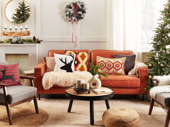 Woonkamer in kerststijl met een oranje bank, kleurrijke kussens, een ronde jute poef en een kerstboom.