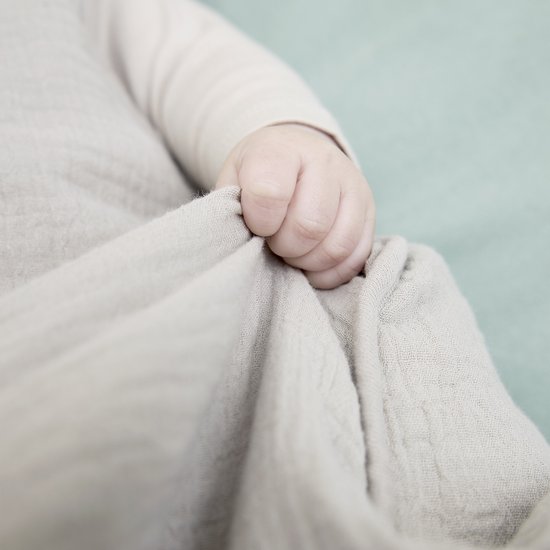 Babyhandje dat de lichtgrijze stof van een Meyco slaapzak vasthoudt.