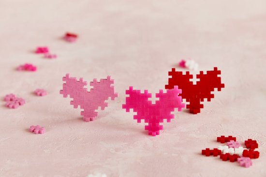 Drie Plus-Plus harten in het roze, fuchsia en rood. Losse rode, roze en witte steentjes liggen verspreid.