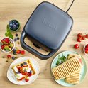 Een gesloten, donkergrijs Tefal wafelijzer staat op een houten aanrecht, omringd door ingrediënten.
