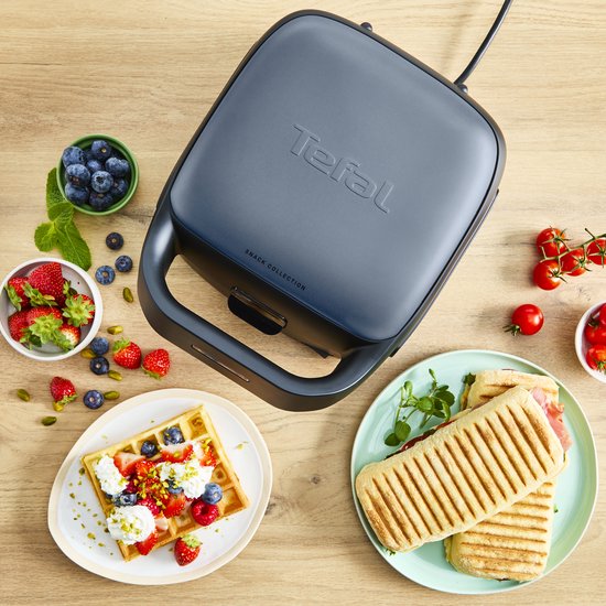 Een gesloten, donkergrijs Tefal wafelijzer staat op een houten aanrecht, omringd door ingrediënten.