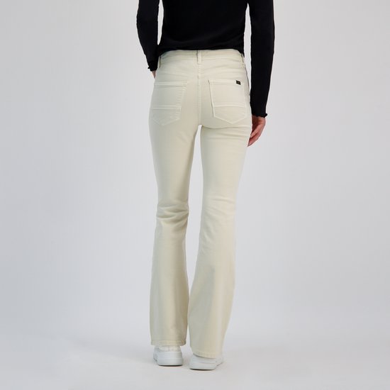 Une femme porte un jean flare en velours côtelé crème. Elle porte un col roulé noir et des baskets blanches.