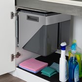 Grijze uittrekbare dubbele afvalbak gemonteerd in een keukenkast, met schoonmaakdoekjes en flessen op de bodem.