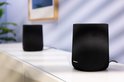 Twee zwarte Harman Kardon speakers op een witte kast, met een gedempte achtergrond.