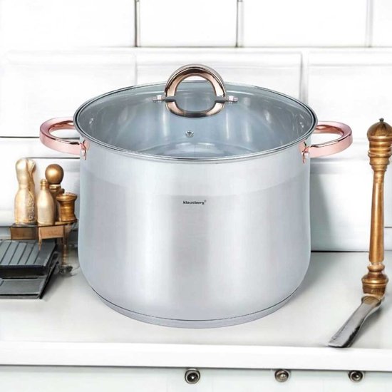 Zilverkleurige soeppan met glazen deksel en koperkleurige handvatten, staand op een aanrecht met keukenaccessoires.