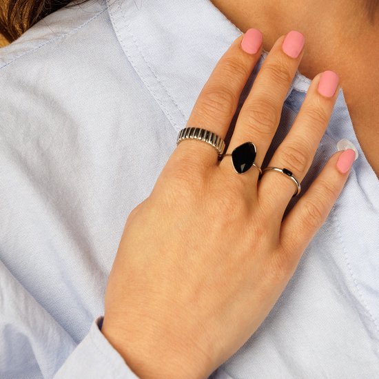 Dameshand met lichtblauwe blouse en roze nagels. Draagt een zilverkleurige ring met facetgeslepen zwarte steen.