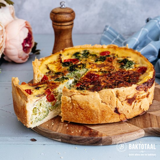 Quiche met broccoli, tomaat en kaas, geserveerd op een houten plank. Een stuk is verwijderd.