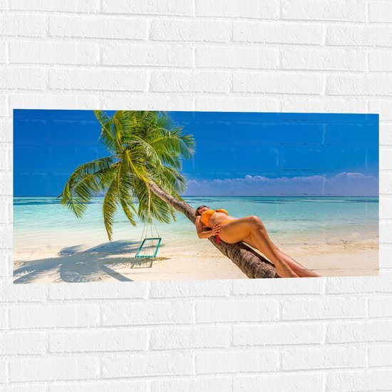 Muursticker - Vrouw in Gele Bikini Liggend op Schuingroeiende Palmboom op Tropisch Strand - 100x50 cm Foto op Muursticker