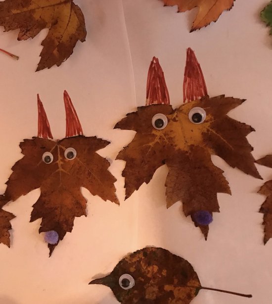 Deux feuilles d'automne décorées comme des visages avec des yeux mobiles, des oreilles pointues rouges et des nez pompons violets.