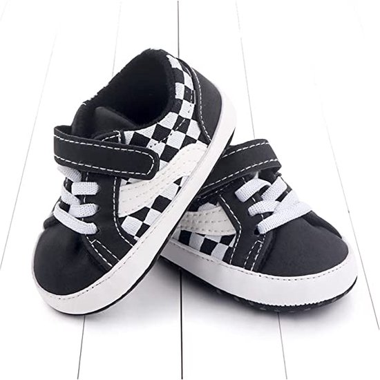 Paar zwarte babyschoentjes met dambordpatroon, klittenbandsluiting en witte veters.