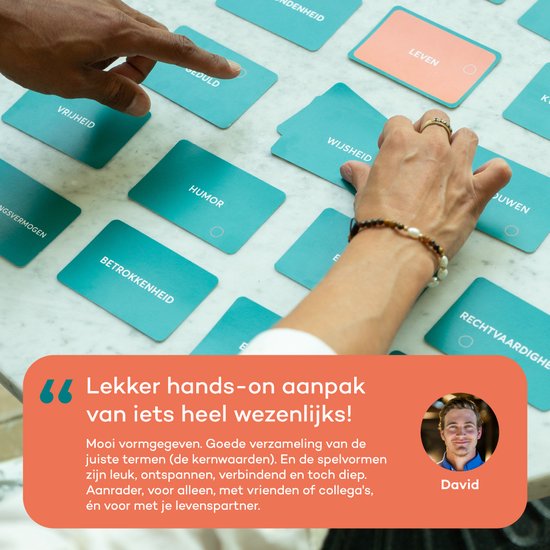 Handen selecteren kaarten van Het Kernwaarden Spel, met focus op woorden zoals "HUMOR" en "WIJSHEID".
