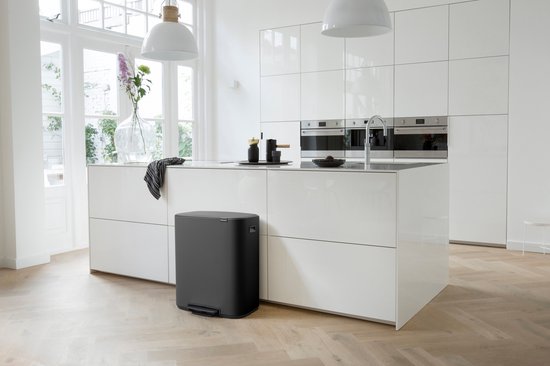 Donkergrijze Brabantia prullenbak op een modern wit keukeneiland, naast een kraan en keukenapparatuur.