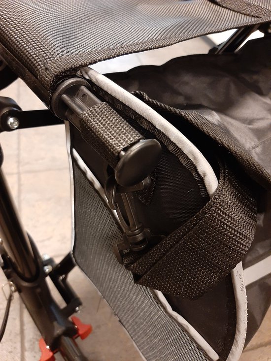 Detailopname van de bevestiging van een zwarte rollatortas aan een rollator met een klittenbandlus.