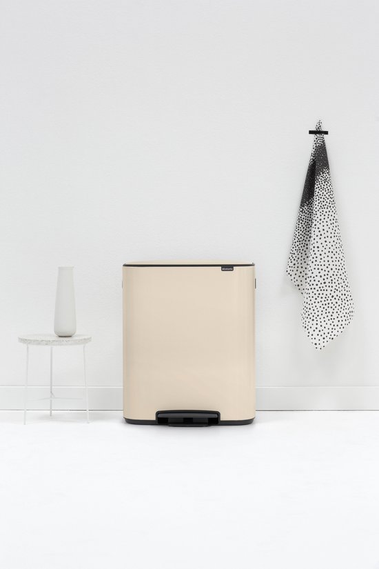 Poubelle Brabantia Bo crème de 60 litres à côté d'une table d'appoint blanche avec un vase.