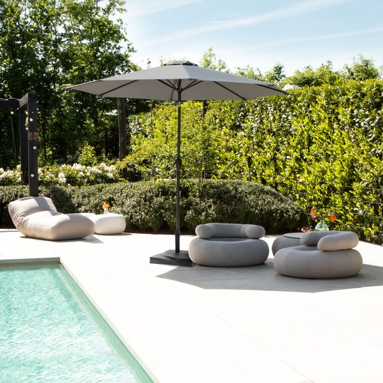 Grijze parasol, open, met een zonnebedje en zitje bij een zwembad.