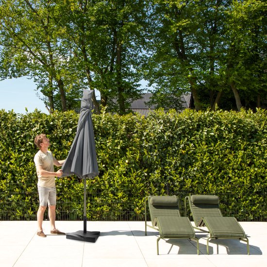 Man vouwt een grijze parasol op bij een zwembad en loungeset.