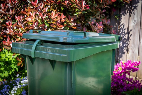 Groene afvalcontainerclip "GREENCLIP" op een groene afvalcontainer in een tuin met bloemen.