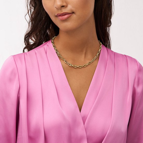 Model draagt een gouden ketting met ankerschakels om de hals, over een roze jurk.