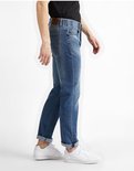 Man van opzij in een lichtblauwe jeans met opgerolde broekspijpen, gedragen met witte sneakers.