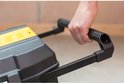 Hand pakt de uitschuifbare handgreep van een zwarte Stanley gereedschapskoffer met gele details.