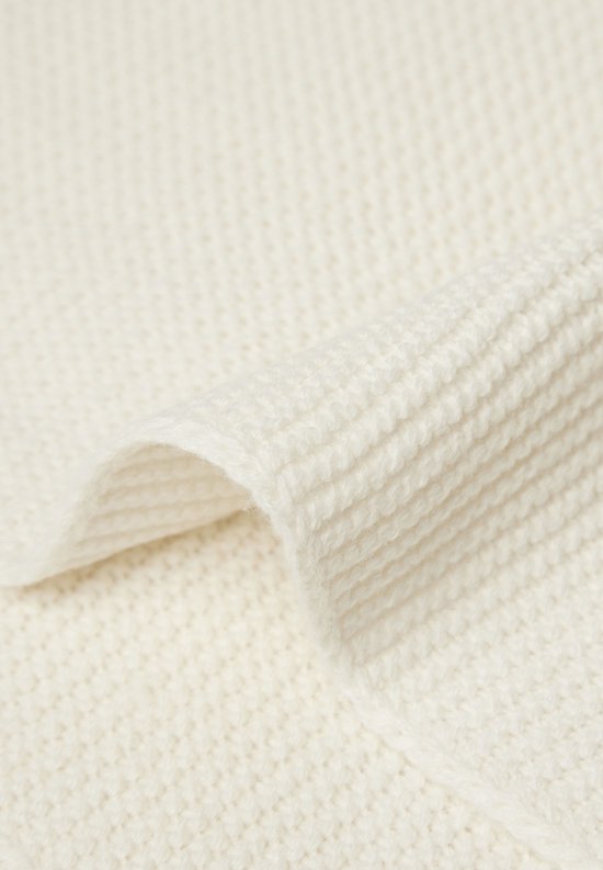 Gros plan de la texture détaillée d'une couverture en maille crème.