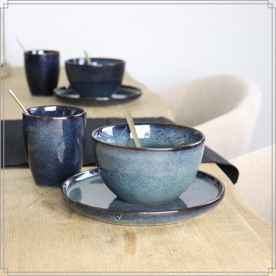 Set van blauwe mokken en kommen met gouden lepels op een houten tafel.