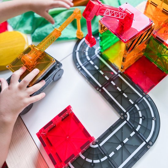 Kinderhanden spelen met Magna-Tiles constructiespeelgoed, inclusief een hijskraan, wegen en kleurrijke transparante bouwblokken.