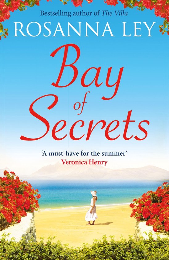 Couverture du livre 'Bay of Secrets' par Rosanna Ley. Une femme en robe d'été blanche et chapeau se tient sur une plage ensoleillée, entourée de fleurs rouges, avec la mer en arrière-plan.