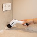 Hand gebruikt de witte elektrische schrobborstel om een aanrecht schoon te maken.