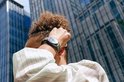 Persoon met groene smartwatch om de pols, met een gebouw op de achtergrond.
