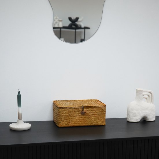 Une boîte de rangement en rotin avec couvercle et fermeture à bouton en bois est posée sur une commode noire, avec un miroir au-dessus.