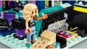 Meisje met blonde krullen in zwart T-shirt met gameprint, grijze broek en sneakers, wijzend naar een spelcomputer.