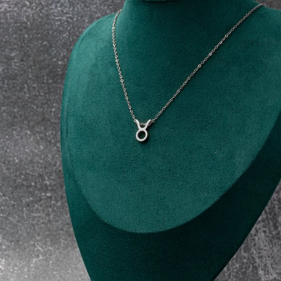 Zilverkleurige ketting met Taurus (Stier) symbool hanger, gedragen op een groene fluwelen display.
